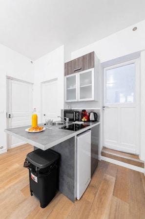 Eine moderne Küche mit grauer Arbeitsplatte, einem schwarzen Mülleimer, einem weißen Kühlschrank und einem Fenster mit Blick.