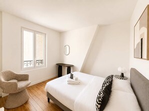 Ein Schlafzimmer mit Bett, Stuhl, kleinem Tisch und einem Fenster mit Jalousien.
