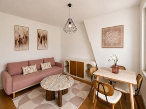 Ein modernes Wohnzimmer mit einem rosa Sofa, einem runden Couchtisch, einem Esstisch mit Stühlen und Kunstwerken an den Wänden.