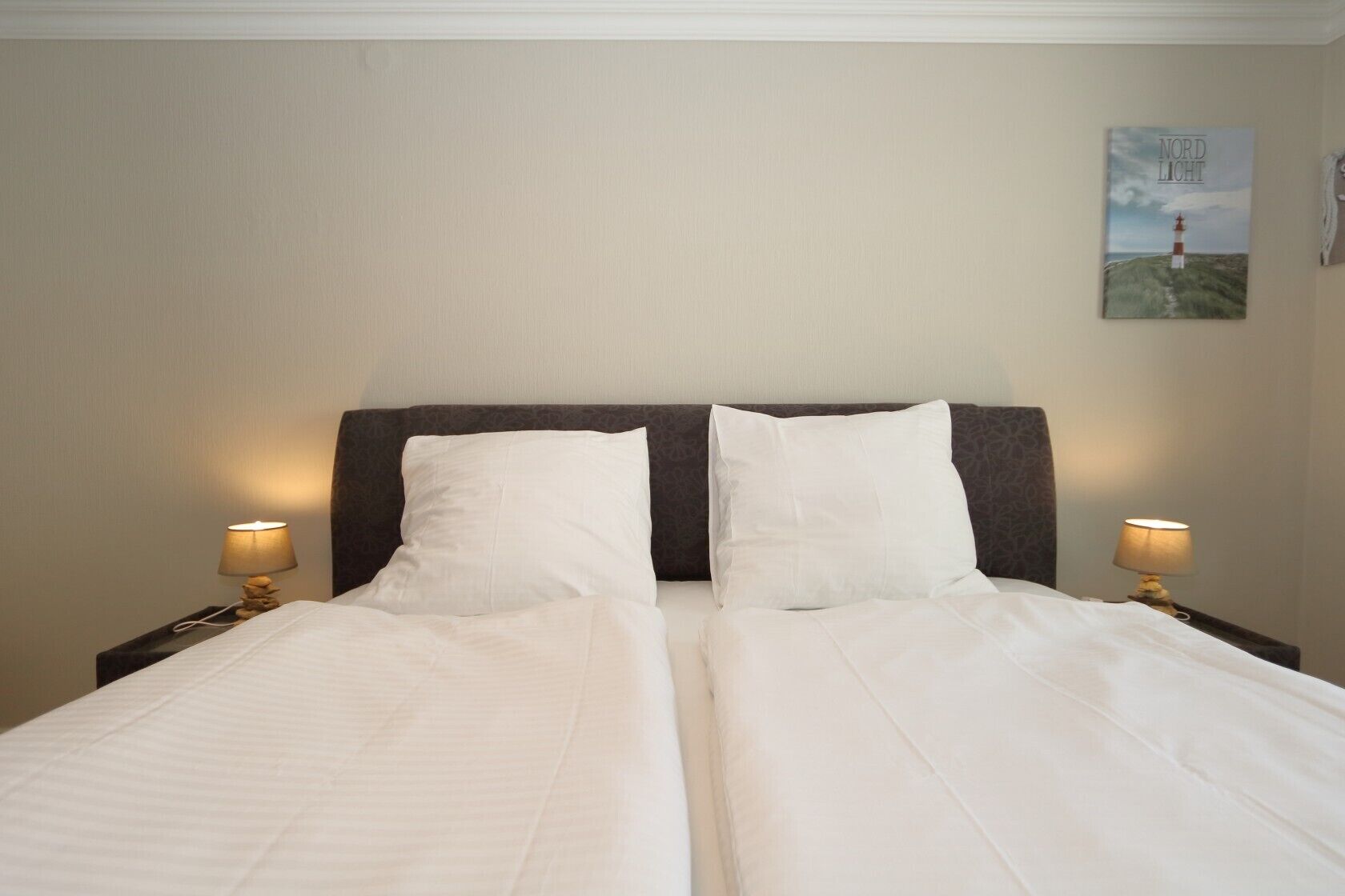 A double bed with white linens, two bedside lamps, and a framed picture on the wall.