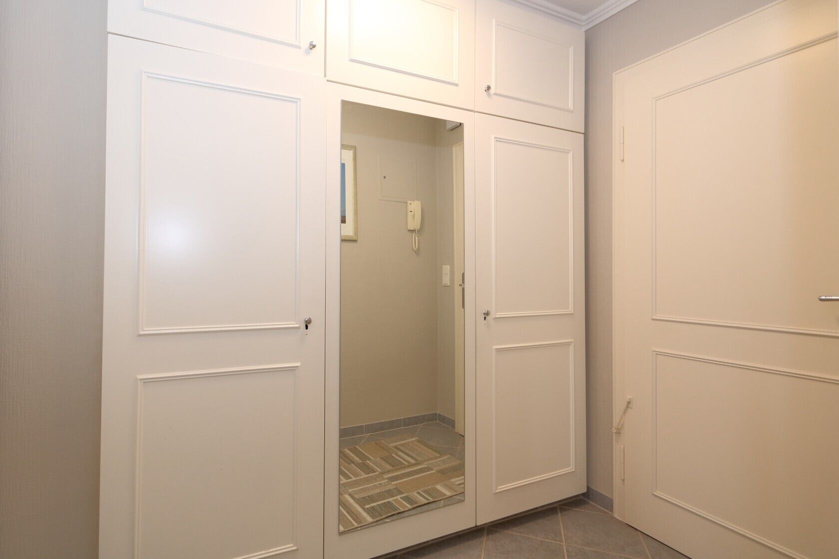 A hallway with white double doors, a tiled floor, and a visible electrical outlet on the wall.