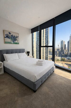 A modern bedroom with a large bed, a nightstand, a lamp, and a painting. - Skyline Stays Southbank Rooftop Pool Apt (Southbank)