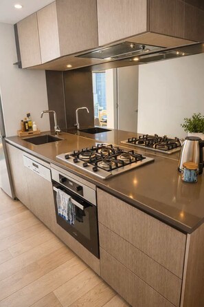 A modern kitchen with a central island, stainless steel appliances, and a built-in oven. - Skyline Stays Southbank Rooftop Pool Apt (Southbank)