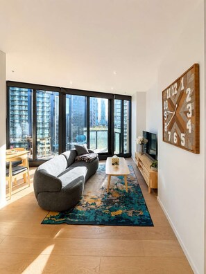 A modern living room with a sofa, coffee table, and a large wall clock. - Skyline Stays Southbank Rooftop Pool Apt (Southbank)