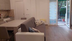 Ein kompakter Wohnbereich mit Küchenzeile, Essbereich, einer Couch und einer Glasschiebetür zu einem Außenbereich.