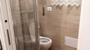 Ein Badezimmer mit Duschkabine aus Glas, Toilette und Fenster mit Spitzenvorhängen.