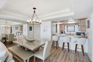 A modern kitchen with a central island, bar stools, and a dining area with a large table and chairs. - Watercrest 1404 - Free Beach Chairs! (Panama City)