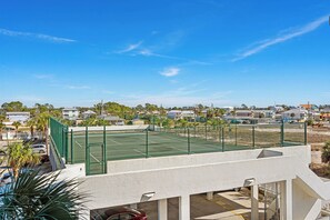 Ein Tennisplatz mit grünem Zaun, umgeben von Wohnhäusern und Palmen.