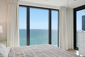 A bedroom with a large window, a bed, a dresser, and a view of the ocean. - Watercrest 1404 - Free Beach Chairs! (Panama City)