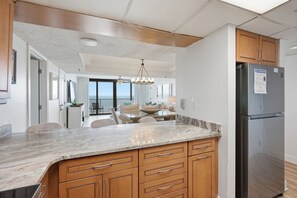 A modern kitchen with a marble countertop, wooden cabinets, and a stainless steel refrigerator. - Watercrest 1404 - Free Beach Chairs! (Panama City)