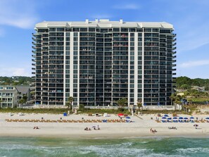 A multi-story hotel with balconies, a beach in the foreground, and a clear sky. - Watercrest 1404 - Free Beach Chairs! (Panama City)