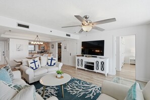 A spacious living room with a ceiling fan, a flat-screen TV, and a dining area with a kitchen in the background. - Watercrest 1404 - Free Beach Chairs! (Panama City)