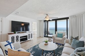A modern living room with a flat-screen TV, a ceiling fan, and a balcony with a view of the ocean. - Watercrest 1404 - Free Beach Chairs! (Panama City)