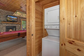 A wooden interior with a pool table, a fireplace, a television, and a washer-dryer unit. - Crazy Horse (Sevierville)