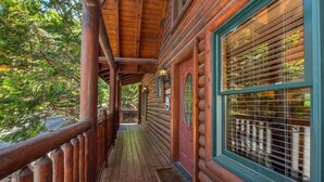 A wooden cabin with a covered porch, large windows with shutters, and a wooden railing. - Crazy Horse (Sevierville)