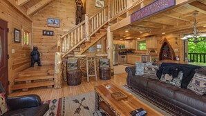 A wooden cabin interior with a staircase, a sofa, a dining table, and a kitchen area. - Crazy Horse (Sevierville)