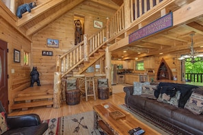 A wooden cabin interior with a staircase, a sofa, a dining table, and a kitchen area. - Crazy Horse (Sevierville)