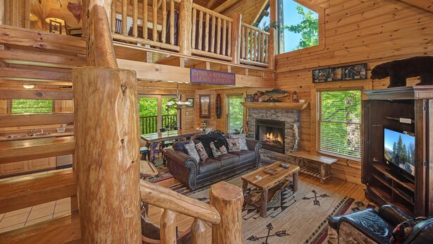 A spacious log cabin interior with a fireplace, a television, a couch, and a dining area. - Crazy Horse (Sevierville)