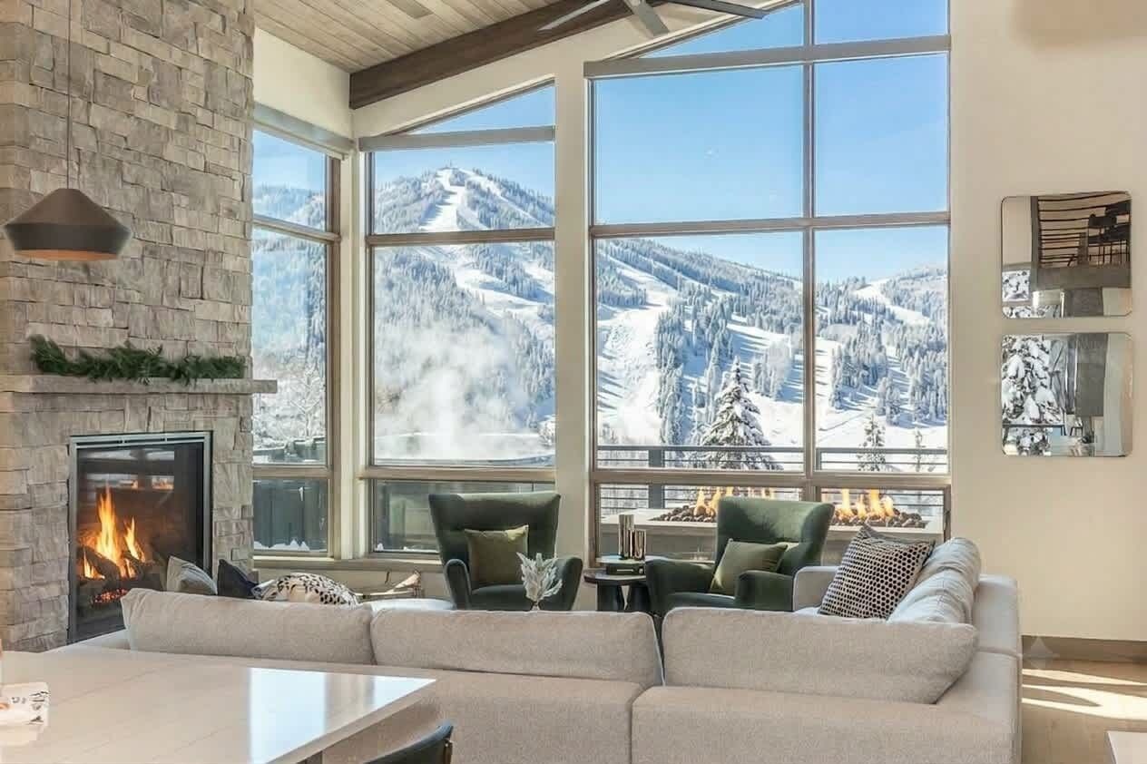 Un salon chaleureux avec une cheminée et de grandes fenêtres donnant sur un paysage montagneux enneigé.