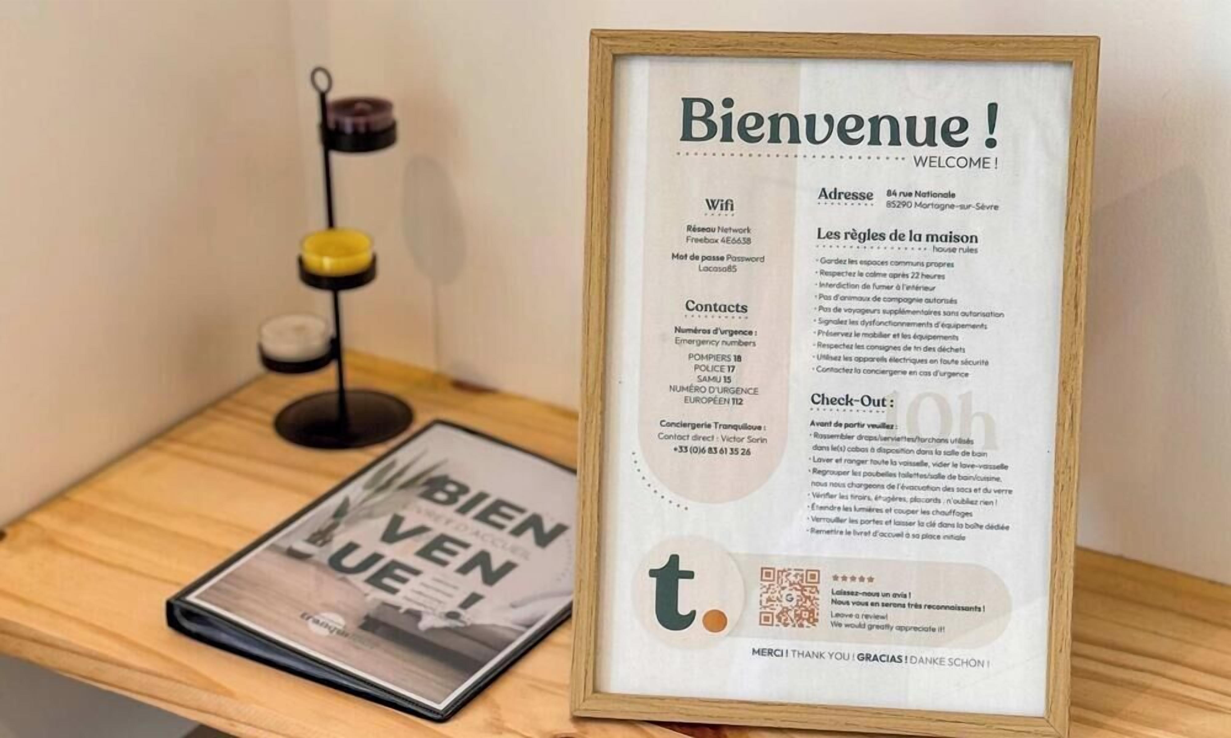 A framed welcome sign with contact information and a QR code, placed on a wooden table next to a magazine.