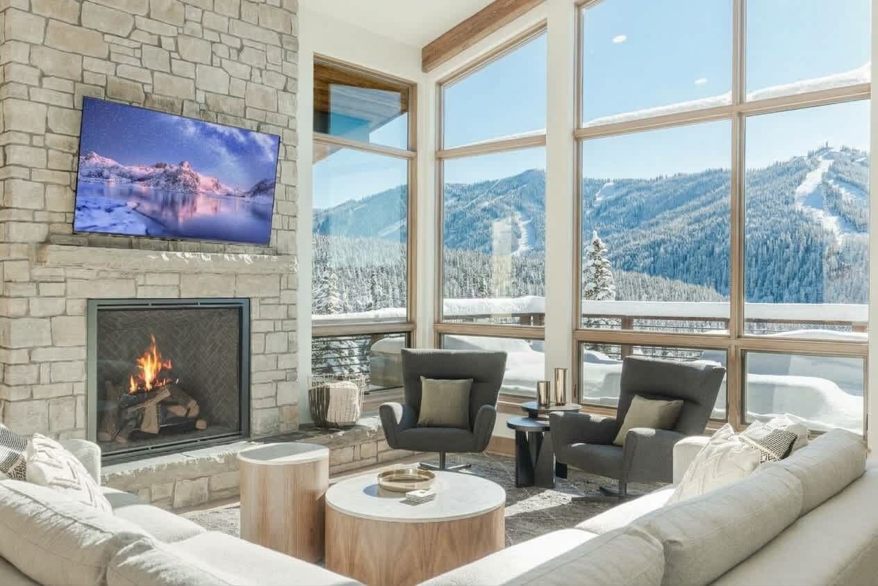A modern living room with a fireplace, comfortable seating, a television, and large windows offering a mountain view.