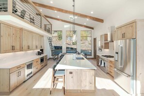 A modern kitchen with wooden cabinets, stainless steel appliances, a central island, and large windows. - First Tracks. Luxury Ski Estate & Rooftop Sauna (Winter Park)