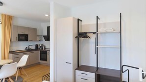 Ein kompaktes Hotelzimmer mit Küchenzeile, einem Bett, einem Schreibtisch mit Schubladen und einem Kleiderschrank.