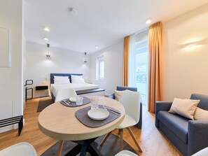 Ein modernes Hotelzimmer mit einem Bett, einem Esstisch mit Stühlen, einer Couch und einem großen Fenster mit Vorhängen.