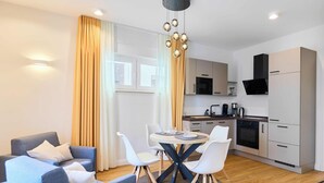 Eine moderne Küche mit Mikrowelle, Herd und Kaffeemaschine, ein Essbereich mit rundem Tisch und Stühlen sowie eine Wohnbereich mit Sofa und Vorhängen.
