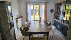 Ruokailutilassa on pitkä pöytä, kuusi tuolia, patteri ja ikkuna, jossa on verhot.