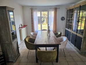 Un coin repas avec une longue table, six chaises, un radiateur et une fenêtre avec des rideaux.