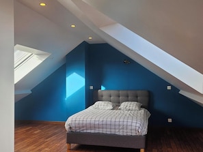 Une chambre avec un plafond en pente, un lit recouvert d’une couverture à carreaux et une lucarne.