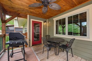 A covered patio with a ceiling fan, a grill, and a table with chairs. - Mountain High (Gatlinburg)
