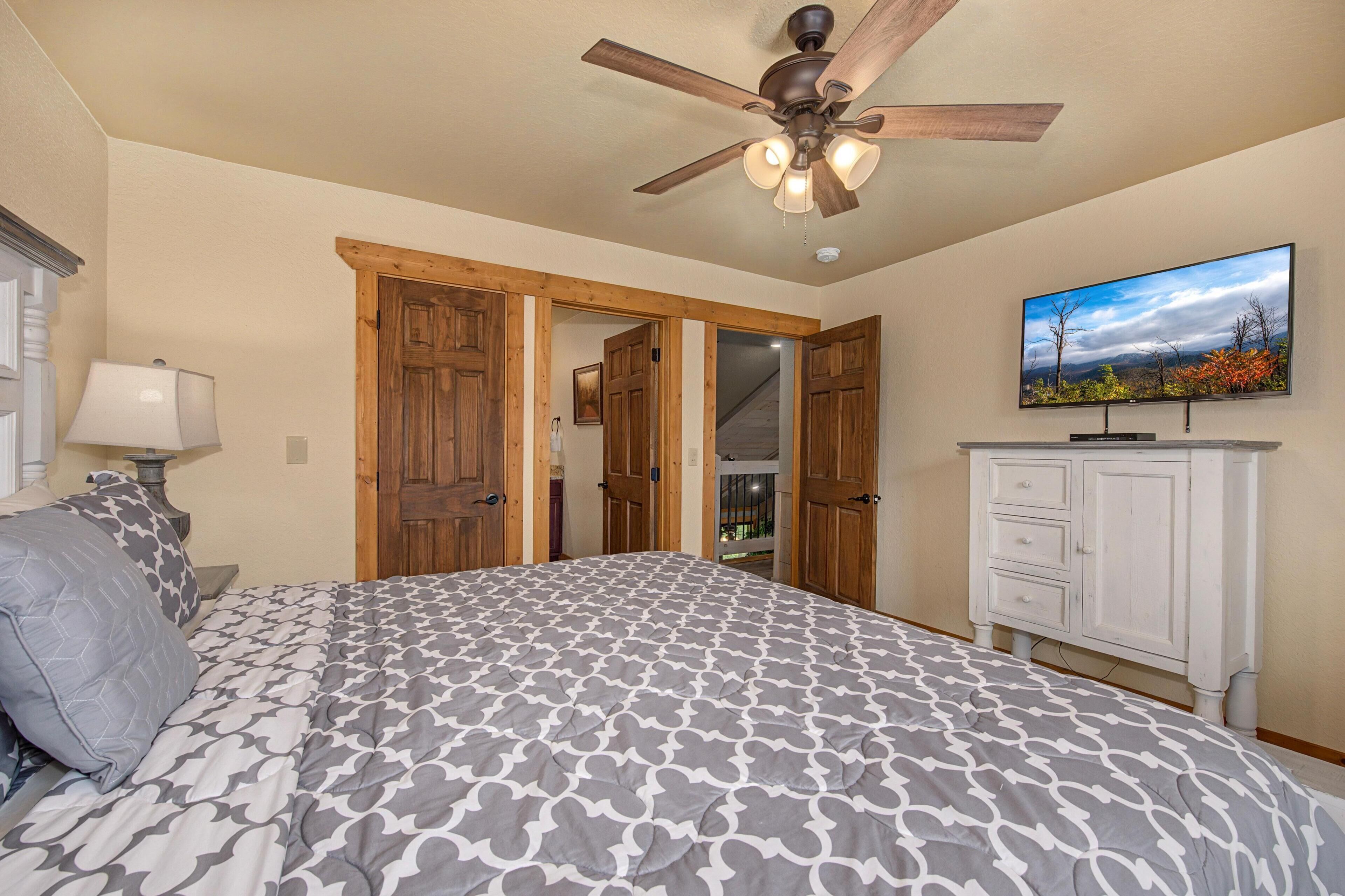 A bedroom with a bed, a ceiling fan, a TV, and a wardrobe.