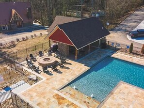 A pool area with a covered seating area, a fire pit, and a stone deck. - Mountain High (Gatlinburg)