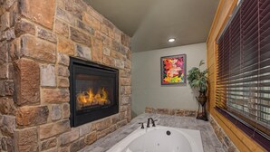 A stone fireplace, a large bathtub, and a window with blinds. - Mountain High (Gatlinburg)