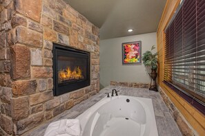 A stone fireplace, a large bathtub, and a window with blinds. - Mountain High (Gatlinburg)