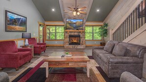 A living room with a fireplace, red and gray sofas, a wooden coffee table, and a ceiling fan. - Mountain High (Gatlinburg)
