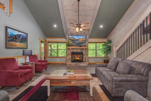 A living room with a fireplace, red and gray sofas, a wooden coffee table, and a ceiling fan. - Mountain High (Gatlinburg)