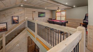 A multi-level room with a pool table, ceiling fan, and wooden walls. - Mountain High (Gatlinburg)