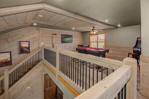 A multi-level room with a pool table, ceiling fan, and wooden walls. - Mountain High (Gatlinburg)
