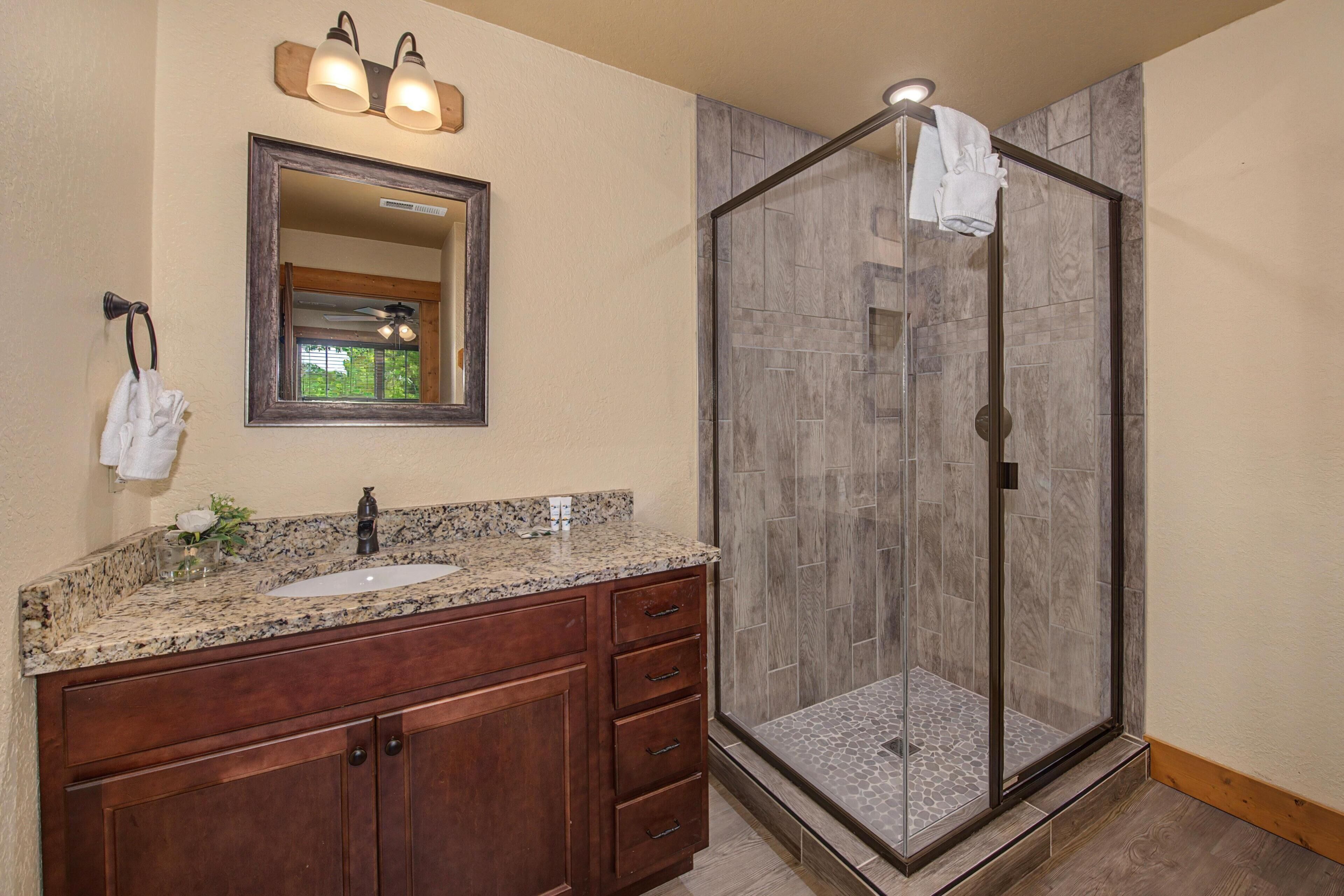 A bathroom with a granite countertop sink, wooden vanity, a large mirror, and a glass-enclosed shower.
