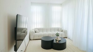 Uma sala de estar moderna com uma grande TV de tela plana, um sofá branco e duas mesinhas de cabeceira pretas.