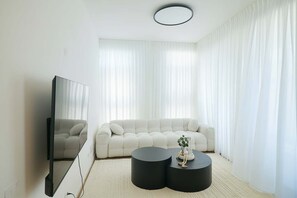 Ein modernes Wohnzimmer mit einem großen Flachbildfernseher, einem weißen Sofa und zwei schwarzen Beistelltischen.