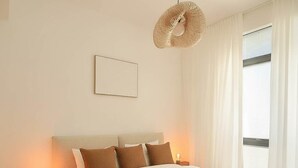 Quarto de hotel com cama, mesas de cabeceira, luminária pendente e janela com cortinas.