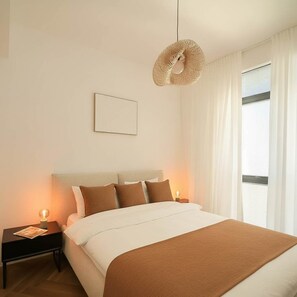 Ein Hotelzimmer mit Bett, Nachttischen, einer Pendelleuchte und einem Fenster mit Vorhängen.