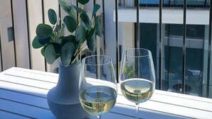 Uma varanda com um vaso de planta e dois copos de vinho branco.