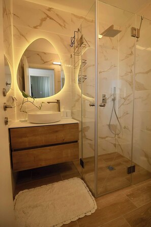 A bathroom with a marble vanity, a glass-enclosed shower, and a mirror with a circular frame. - High-End 1BR in Secure Tower | Parking | Mamak (Tel Aviv-Yafo)
