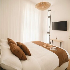 A bedroom with a bed, a television, a bedside table, and a window with curtains. - High-End 1BR in Secure Tower | Parking | Mamak (Tel Aviv-Yafo)