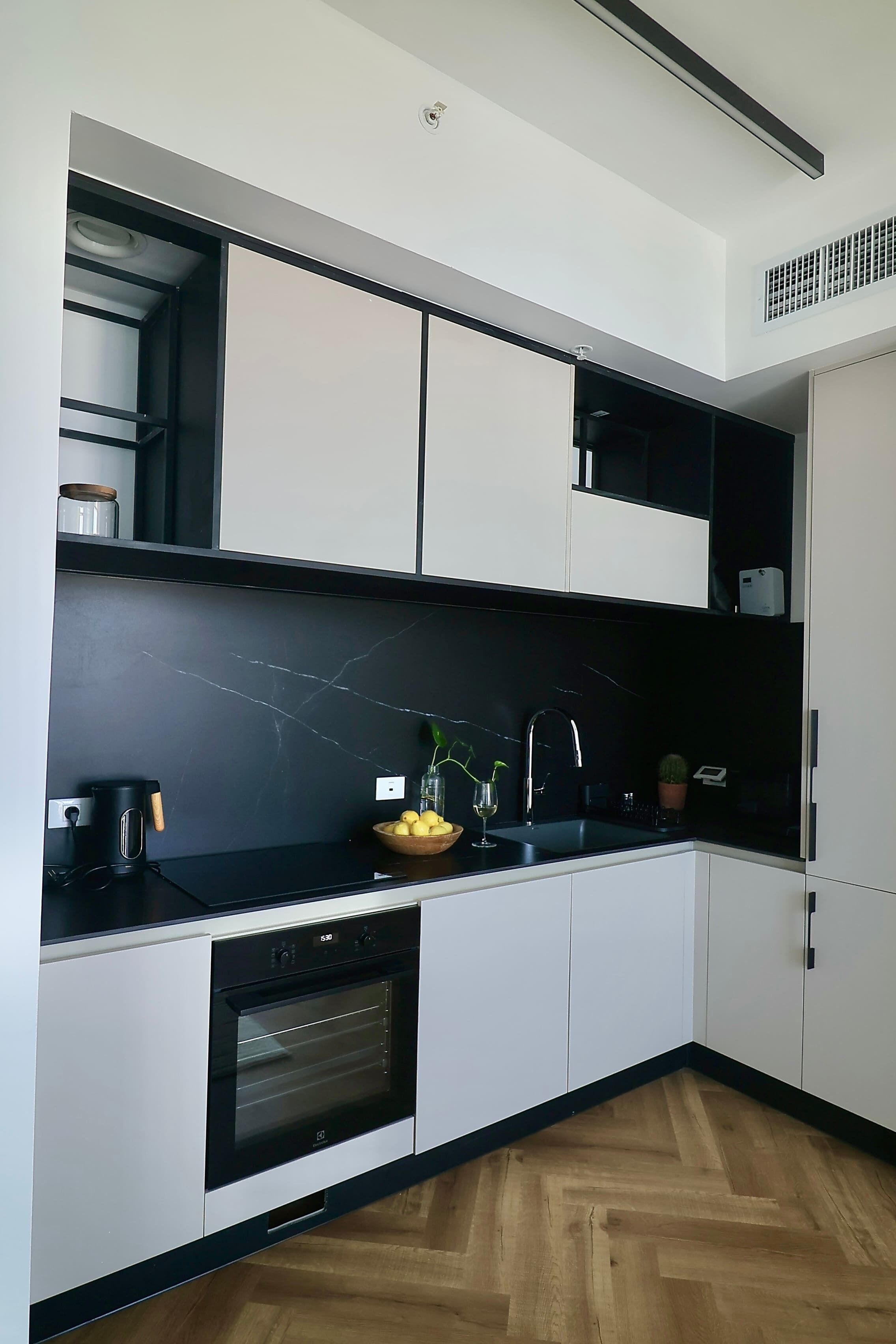 A modern kitchen with white cabinets, a black countertop, a built-in oven, and a black backsplash.
